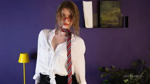 Young woman in white shirt and striped tie posing against a purple wall in a moody indoor setting.