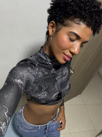 Young woman in a black dragon print turtleneck crop top and blue jeans posing indoors.