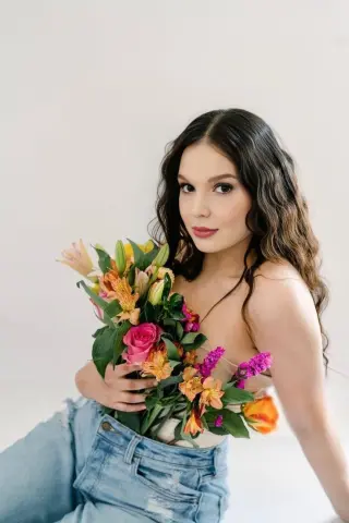 Young woman in denim jeans holding a vibrant colorful flower bouquet against a white background.
