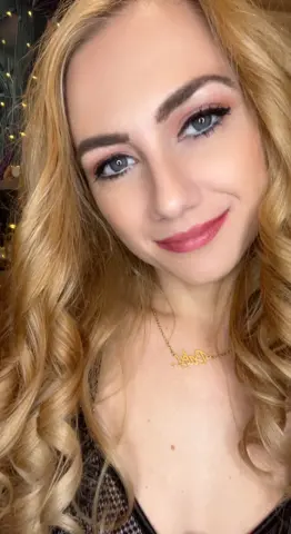GoddessDublinRae smiles at the camera with her long blonde wavy hair and a gold necklace.