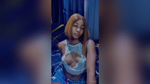 JoanJon wears a white lace crop top and blue shorts while posing in her bedroom.