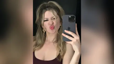 CassieArmas pouts her lips and makes a funny face while taking a mirror selfie in a dark tank top.