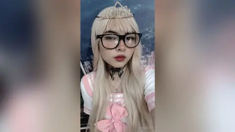 Blonde girl in pink princess cosplay wearing a tiara and black glasses with a dreamy aesthetic.