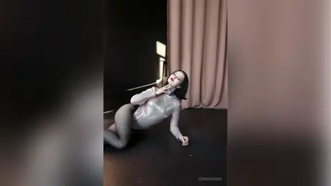 Elegant woman in a shimmering silver long-sleeve bodysuit posing gracefully in a dark studio setting.