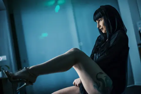 Moody portrait of a woman in a black outfit sitting in a dimly lit blue room.
