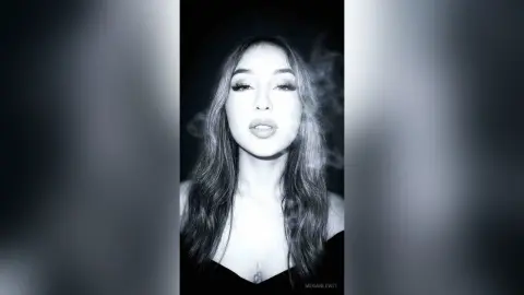 MeganLewit poses with long dark hair and smoky eyes against a dark background.