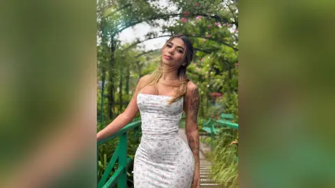 Young woman in a white floral sundress posing in a lush green garden setting with a serene mood.