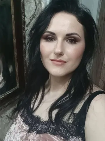 SweetEmmyGirl poses with long black hair and heavy eye makeup, wearing a black lace camisole or tank top.