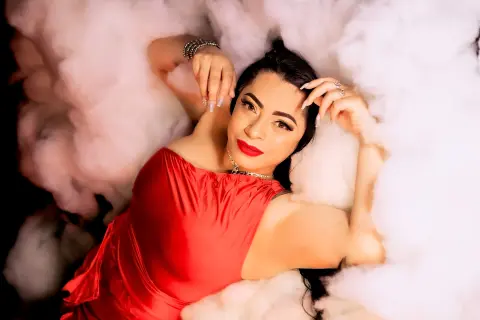 Glamorous woman in a red satin dress lying amidst soft white clouds for a dreamy, romantic photoshoot.