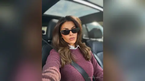 Stylish woman in a mauve sweater and black sunglasses sitting in a car with a relaxed mood.