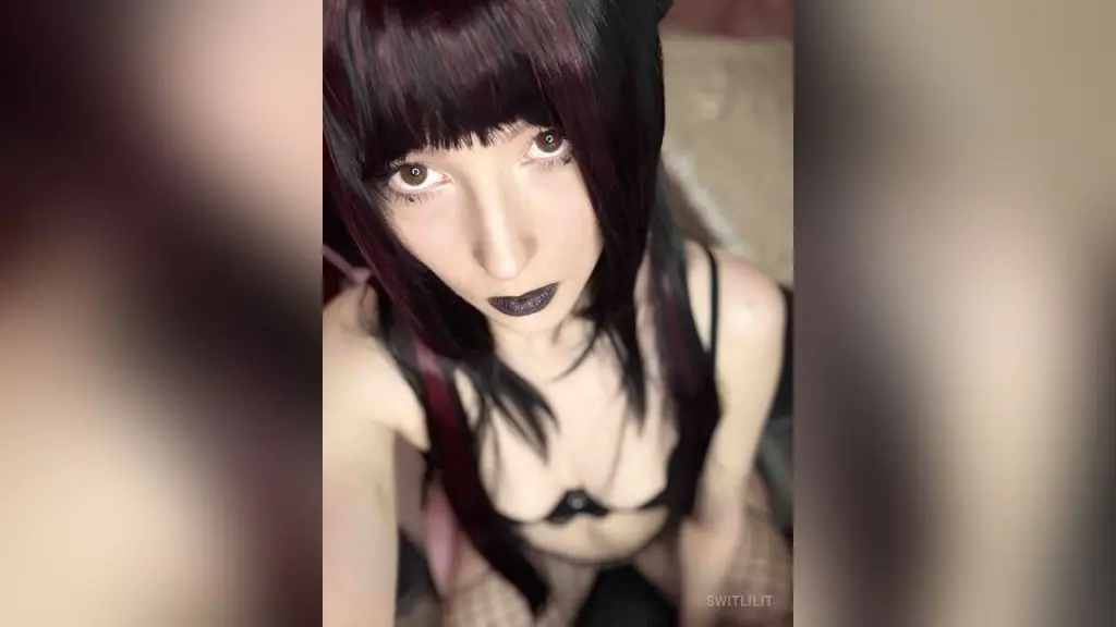 SwitLilit — Young woman with dark hair and dark lipstick wearing black lingerie in a soft-lit indoor setting.