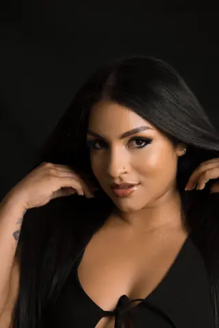 Beautiful woman with long dark hair and nose ring wearing a black top in a moody studio setting.