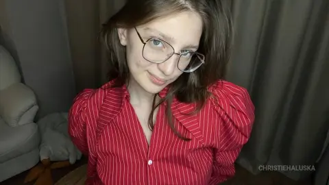 Young woman with glasses wearing a red striped puff-sleeve blouse in a cozy indoor setting.
