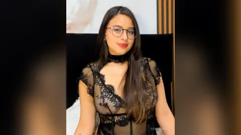 Young woman with glasses in a black lace bodysuit sitting in a modern interior setting with a confident mood.