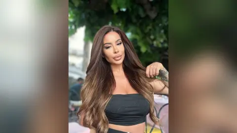 ReynaGomes poses outdoors with long, wavy brown hair, wearing a black tube top.