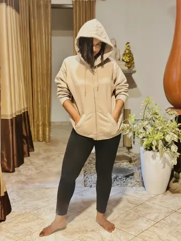 Angel_Myurs — Angel_Myurs stands in a room wearing a tan hoodie and black leggings with her hair covering part of her face.