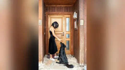 MichaelaBelle stands in a wooden doorway wearing a black tank top and skirt while petting a black dog.