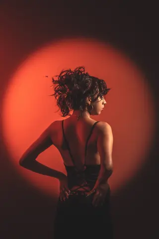 Elegant woman in a black backless dress posing against a dramatic red spotlight background.