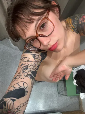 Isabella_Stewart wears brown glasses and shows her heavily tattooed arms while looking at the camera.