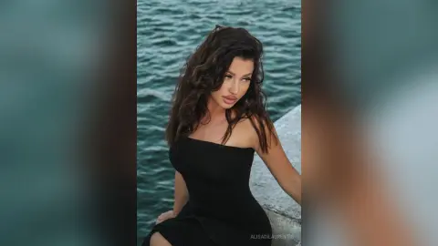 Elegant woman in a black strapless dress posing by the ocean during a moody sunset.