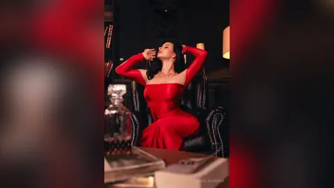 Elegant woman in a red evening gown posing in a moody, dark luxury library setting.