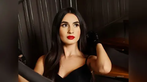 Elegant woman in a black dress and lace gloves posing with a glamorous look on a dark staircase.