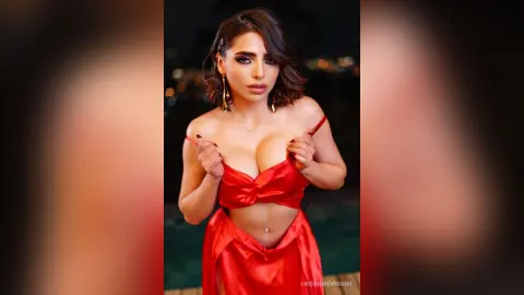 Glamorous woman in a red satin outfit posing at a night poolside setting with a sultry mood.