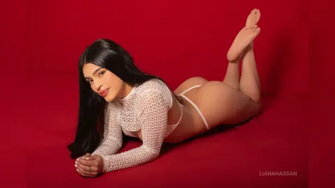 Beautiful woman with long dark hair in white lace lingerie lying on a red background.