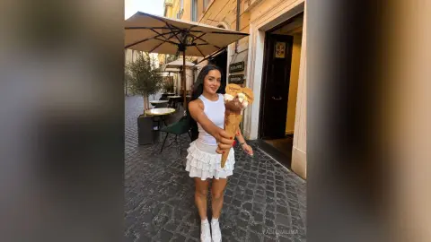 FabianaLima stands on a cobblestone street wearing a white tank top and a white ruffled skirt while holding a large ice cream cone.