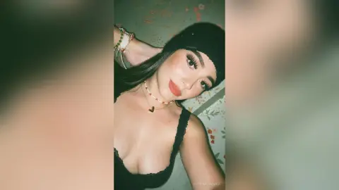 Young woman in a black tank top and black beanie posing with a soft, glowing aesthetic against a floral background.