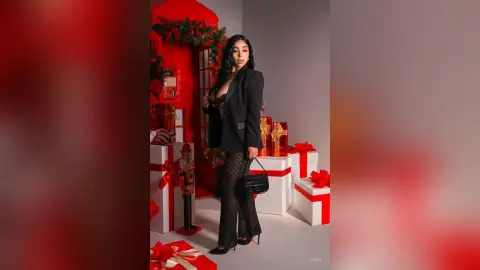 Stylish woman in a black blazer and patterned trousers posing with red and white Christmas gifts in a festive setting.