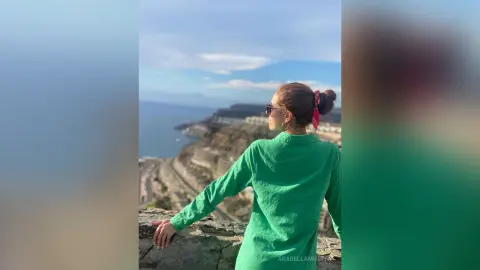 Woman in a green linen shirt looking at the ocean from a scenic coastal cliffside viewpoint.