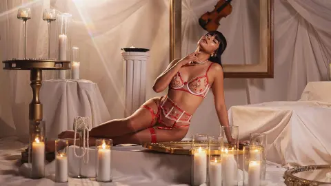 Elegant woman in red lace lingerie relaxing in a romantic candlelit bedroom setting.