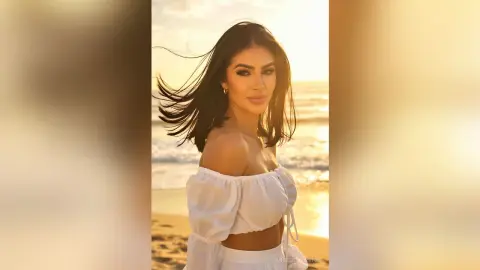 Beautiful woman in a white off-the-shoulder top enjoying a golden sunset on a breezy tropical beach.