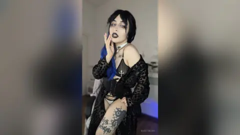 Gothic woman with dark makeup and black lace outfit posing in a moody indoor setting.