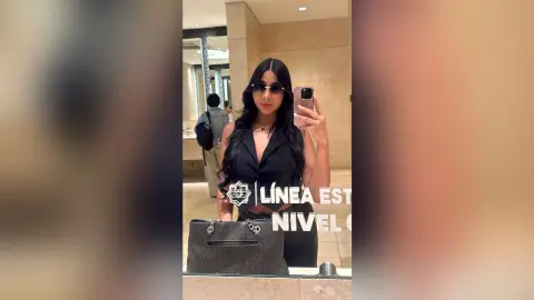 KimberlyIsaza poses for a mirror selfie wearing a black sleeveless top and sunglasses, holding a phone with her long dark hair down.