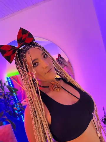 Blonde woman with long braids and a red checkered bow wearing a black halter top in moody purple lighting.
