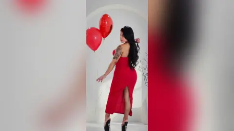 Elegant woman in a red evening gown posing with red balloons in a bright, minimalist studio setting.