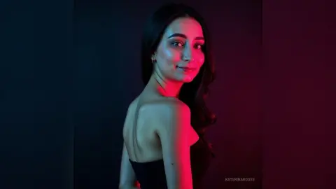 Elegant woman in a black strapless dress posing with moody red and blue studio lighting.