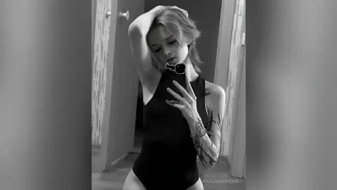 PaulinaCundiff poses in a black bodysuit, holding her phone for a mirror selfie while showing off her tattoos.