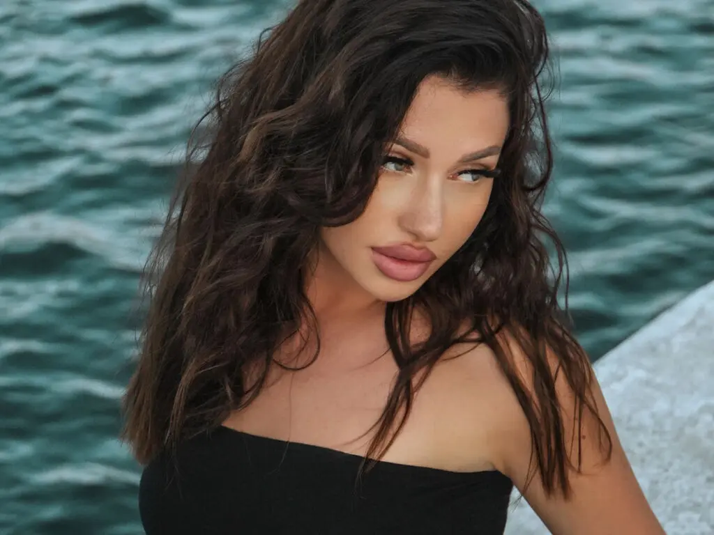 Brunette woman in a black strapless top posing with a serene expression against a turquoise ocean background.