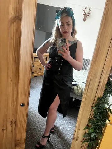 FrankiiRayeXXXX poses in a black sleeveless dress with a high slit, standing in front of a mirror in a bedroom.