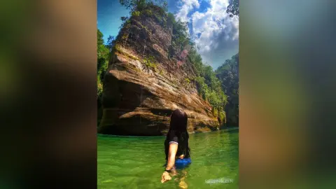 RossiNoleen wades in clear green water against a backdrop of a large, mossy rock cliff.