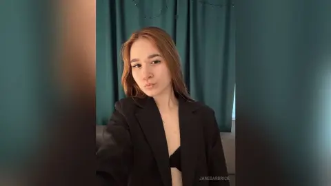 JaneBarbrick poses in a black blazer and black bra against teal curtains.