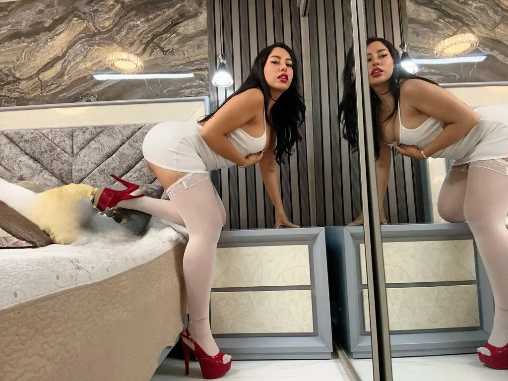 Brunette woman in a white low-cut halter top relaxing in a cozy bedroom setting.