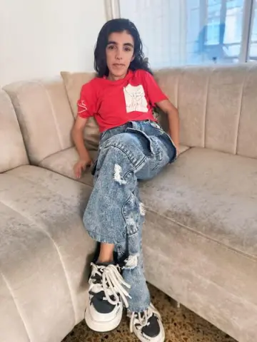 Young woman in red t-shirt and baggy distressed jeans sitting relaxed on a beige sofa.