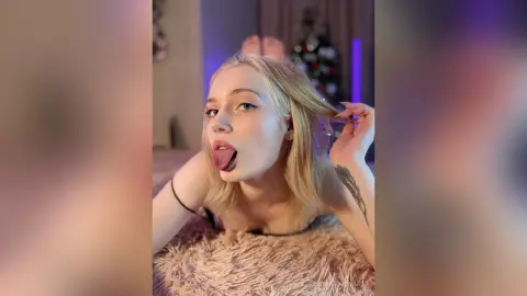 Blonde woman in a black top sticking her tongue out playfully while lying on a fuzzy rug in a dimly lit room.