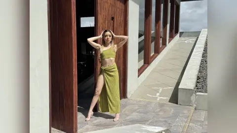 Fashionable woman in a lime green crop top and slit maxi skirt posing by a modern wooden doorway.