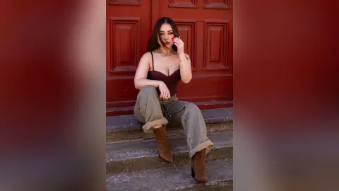 Stylish woman in a burgundy bodysuit and olive cargo pants sitting on steps before a vintage red door.