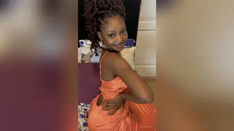 Smiling woman in a peach satin slip dress posing indoors with a joyful expression.